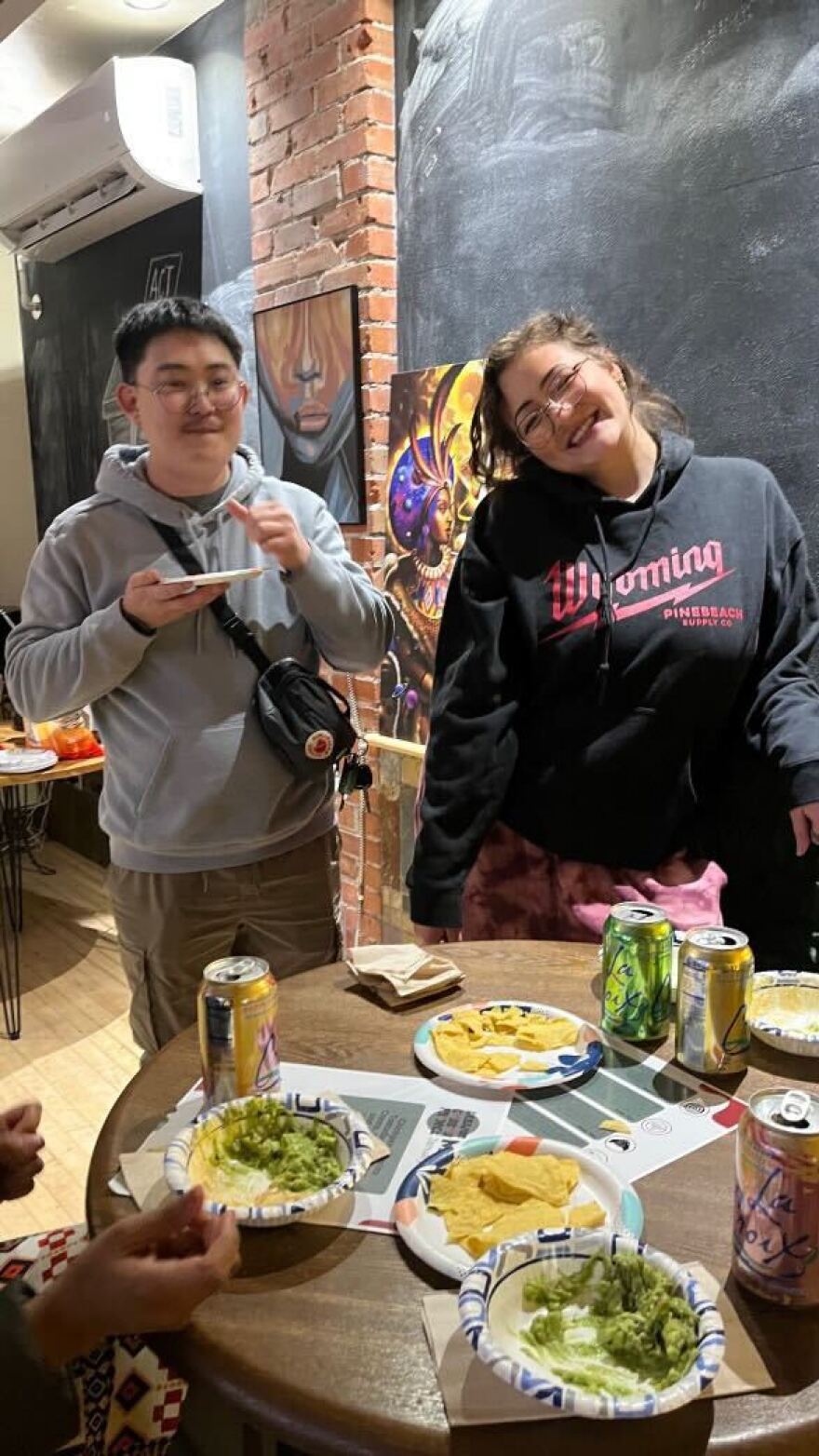 Two people stand behind a table with plates of food and drinks.