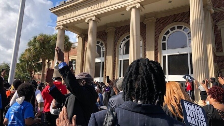 Attendees raise their hands in prayer during a rally outside the Glynn County Courthouse, where the three men accused of murdering Ahmaud Arbery are on trial.