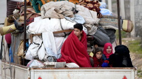 People ride in the back of a truck with furniture, mattresses, and blankets while passing by an internally-displaced persons (IDP) camp near the Turkish border in the west of Syria's northern province of Aleppo on Feb. 16, 2020, fleeing advancing Syrian government forces in Idlib and Aleppo provinces. (Rami al Sayed/AFP/Getty Images)