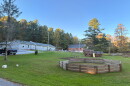 A green mowed yard with a swing-set, a wooden ship with a slide, and a fenced in area, with several building in the background. 