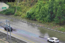 Floodwaters cover lanes of a highway as cars pass.