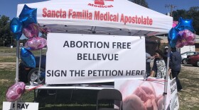  Pink and blue balloons, a picture of a fetus and a sign reading “ABORTION FREE BELLEVUE SIGN THE PETITION HERE” are tied to a white tent. 

