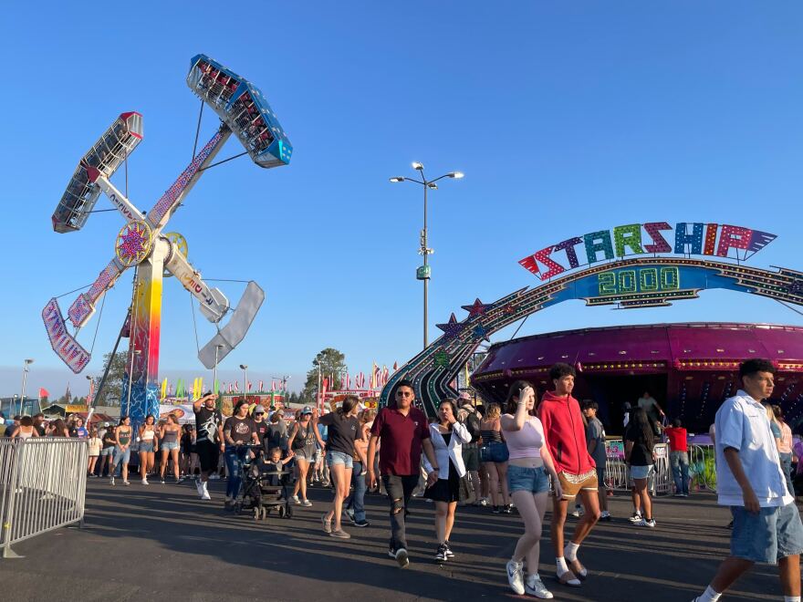 A large crowd walks in front of a colorful sign reading "Starship 2000." Behind it, a large carnival ride's arms are in the air, suspending riders upside down.