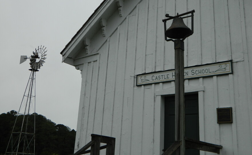Looking up at the Castle Haven School. The post of the school bell at the door obscures the word "Haven" on the sign that hangs above the entrance. A windvane in the background to the left.