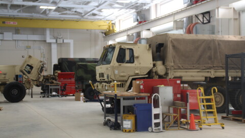 Military vehicles are parked for servicing inside of a National Guard field maintenance shop.