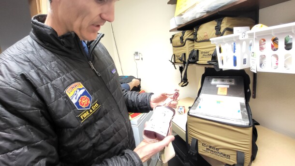 A man holds up a container of blood in a medical room.