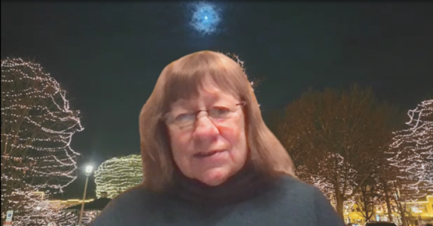 Screenshot of Carol Obertubbesing on Zoom with a background picture that she took of Woodstock Square in Woodstock, Illinois.