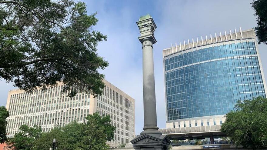 Pedestal in the middle of Hemming Park where a confederate mounment used to be on top, downtown buildings in the background, and the skyrail