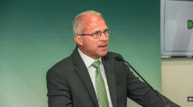 A man in a suit and tie speaks at a small microphone