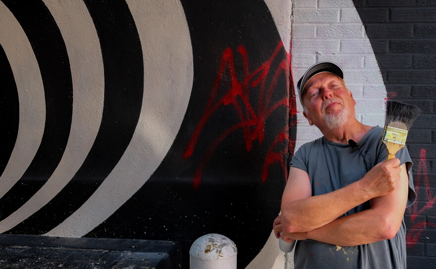 Paul Chelstad stands before a mural he painted at last year's Alley Arts Festival.