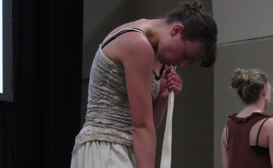 A young woman pulls a long strip of white material out of her mouth