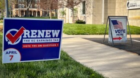 A blue sign with white and red lettering reads "Renew the KC earnings tax. Vote yes on question 1." Another in the background says "vote here"