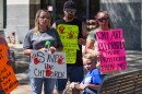 Three adults and a child at a save the children walk in Lima, Ohio. They hold signs that say "save the children" and "Why are pedophiles more protected than me?"