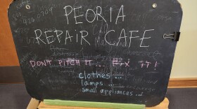 A blackboard that reads "Peoria Repair Cafe. Don't pitch it...Fix it! Clothes, lamps, small appliances."