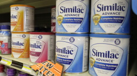 Cans of Similac baby formula sit on a grocery store shelf. The cans are yellow, red and blue. 