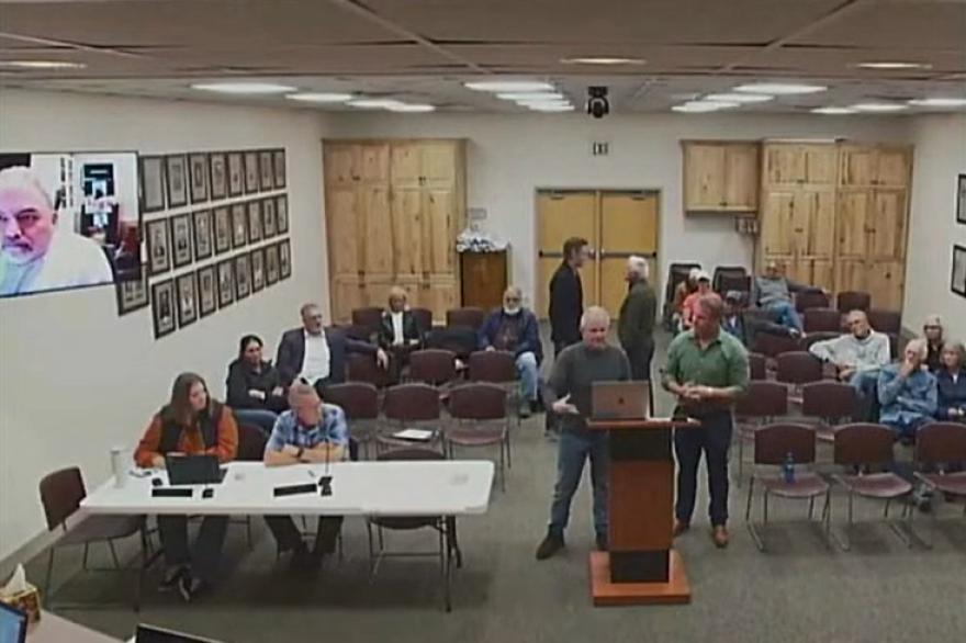 DeJoria Center buyer Shane Starr (left) huddles with High Star Ranch asset manager Gary Raymond (right) before Starr informs the Kamas City Council that he and business partners Mitch Burton and George Wright (at podium) intend to purchase more land in the neighborhood. Attorney Matt Ence joins via video call. Residents watch in the audience.