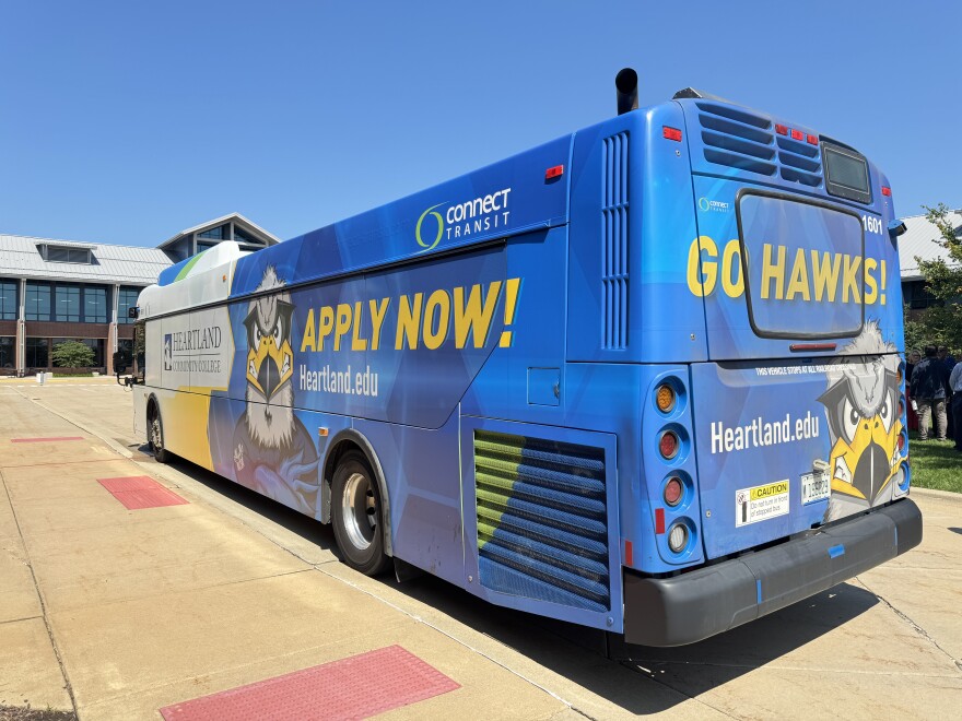 A blue and white bus, that says "apply now" and "go Hawks" with a Hawk on the side and back to promote Heartland Community College.