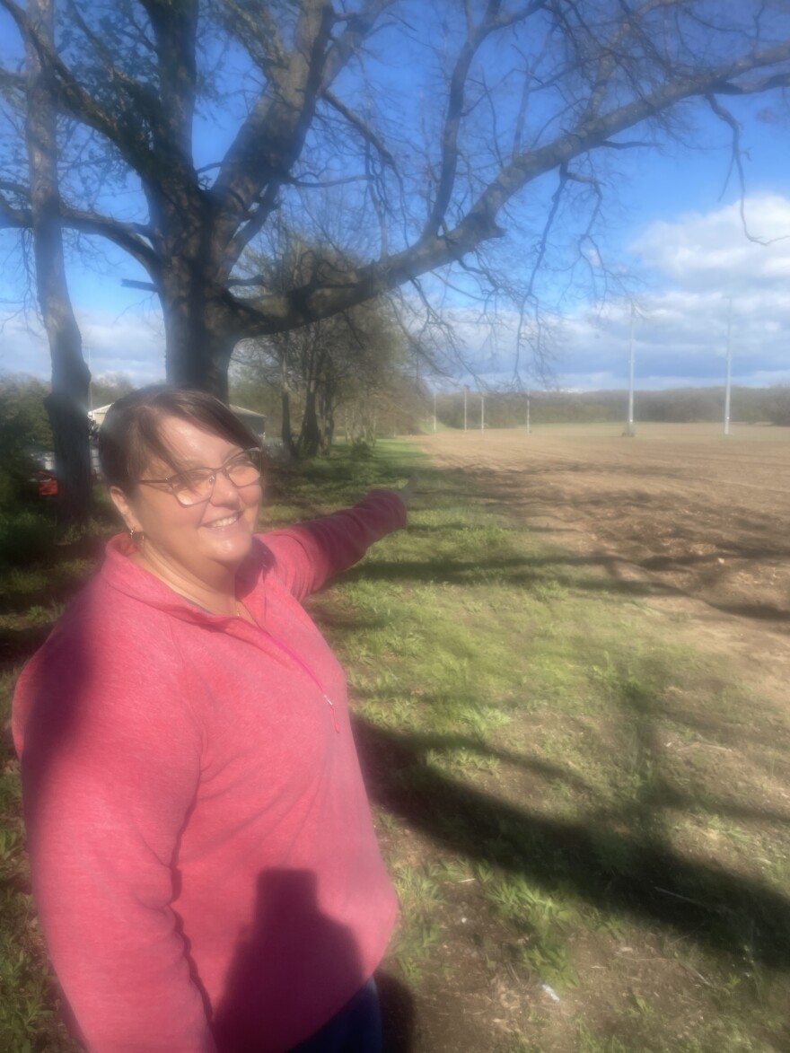 A woman points at power lines with farmland in the background.