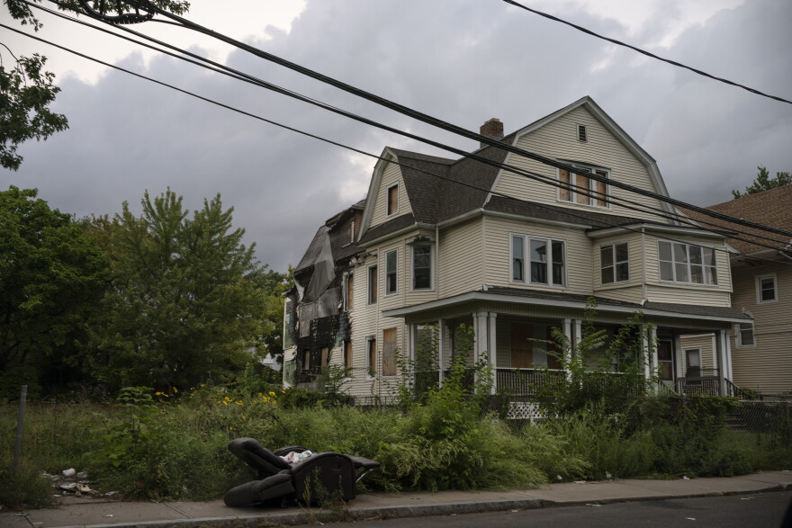 A discarded reclining chair is left on the sidewalk of a residential street in front of a house with a damaged facade in Hartford, Conn., on Tuesday Sept. 13, 2022. A majority of Black residents in Hartford are renters who live in old houses, often suffering from issues like mold and asbestos, which exacerbate health conditions like asthma, particularly for children.