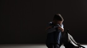 Upset boy with backpack sitting in dark room. Space for text