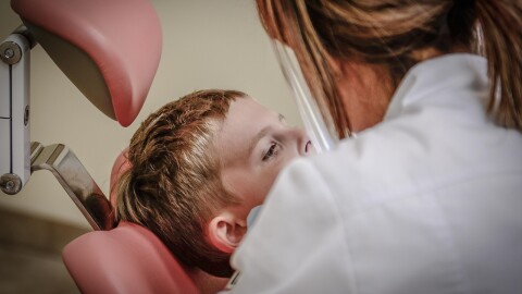 A boy is examined while sitting in a dentist's chair.