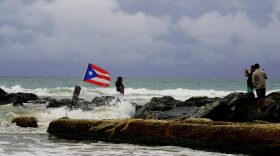 A woman poses for a photo backdropped by ocean waters and a Puerto Rican national flag, after the passing of Tropical Storm Dorian, in the Condado district of San Juan, Puerto Rico, Wednesday, Aug. 28, 2019. The Hurricane Center said the storm could grow into a dangerous Category 3 storm as it pushes northwest in the general direction of Florida. (AP Photo/Ramon Espinosa)