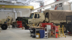 Military vehicles are parked for servicing inside of a National Guard field maintenance shop.