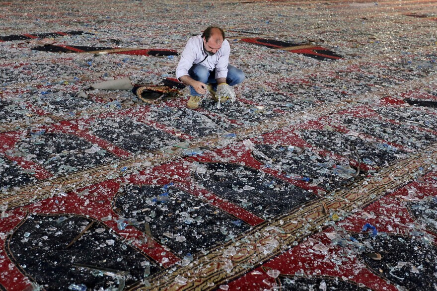 On Wednesday, a man removes broken glass scattered on the carpet of a mosque damaged in Tuesday's blast in Beirut.