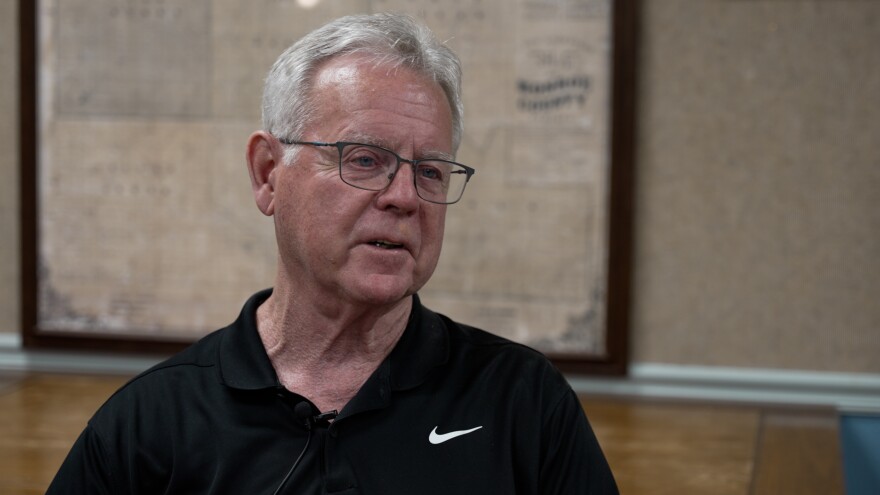 A man wearing black polo shirt sits and talks during an interview