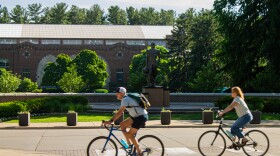 Two people biking across statue.