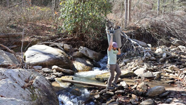 MountainTrue crew member walking a trash can full of debris back to the dumpster on Hickory Creek, Nov. 12, 2025