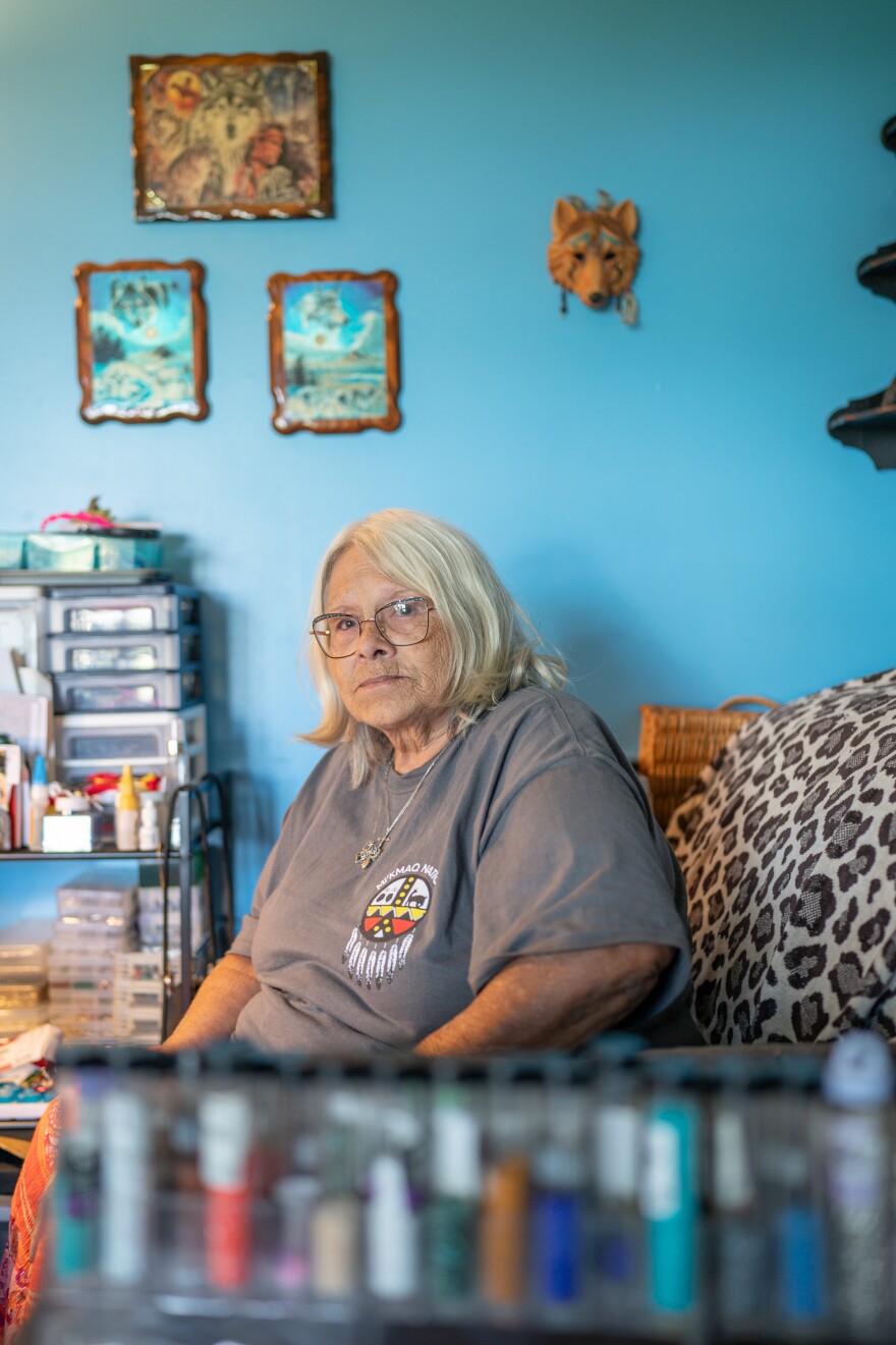 A woman with blonde hair sits on a leopard print patterned seat in front of a bright blue wall inside her home.