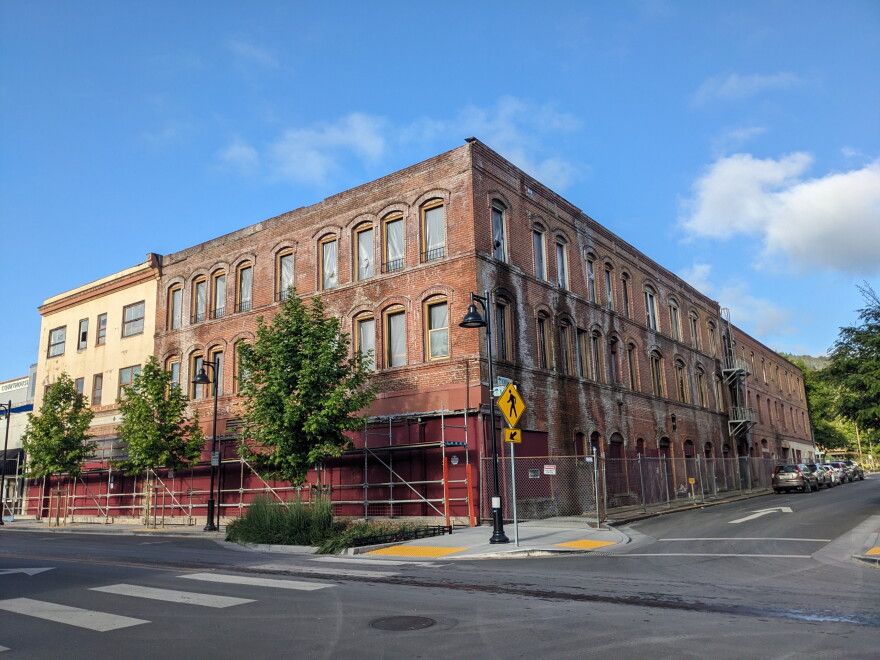 A two-story brick building on a street corner, surrounded by chain link fence and scaffold.
