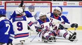 Kevin McKee wears a team USA jersey and is surrounded by other sled hockey players on the ice. 