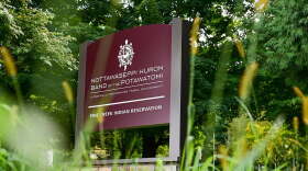 A dark red sign for the Nottawaseppi Huron Band of Potawatomi's Pine Creek Reservation can be seen in a shot that's looking up from the ground. 