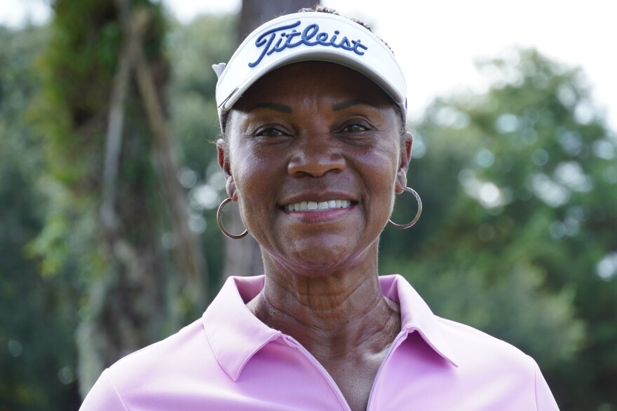 An African American woman wearing a pink shirt and hoop earrings and hat standing outside. 
