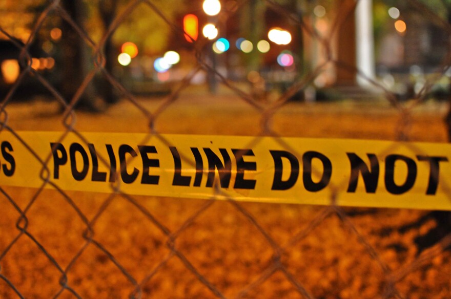 Police tape behind a fence, with lights in the background.