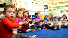 A group of preschoolers sits in a circle singing Alutiiq songs.