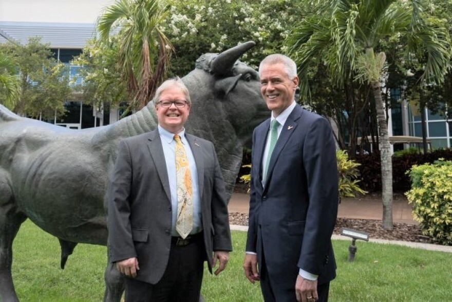 Two men in suits stand in front of a bull statue