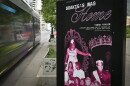 A black and purple sign sits on a city sidewalk. There are several photos of people on it. The sign reads "Soakie's Was Home."