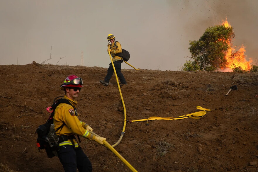 Cal Fire firefighters carry a fire hose up a hillside during the Sandy Fire in Simi Valley on May 18, 2026.