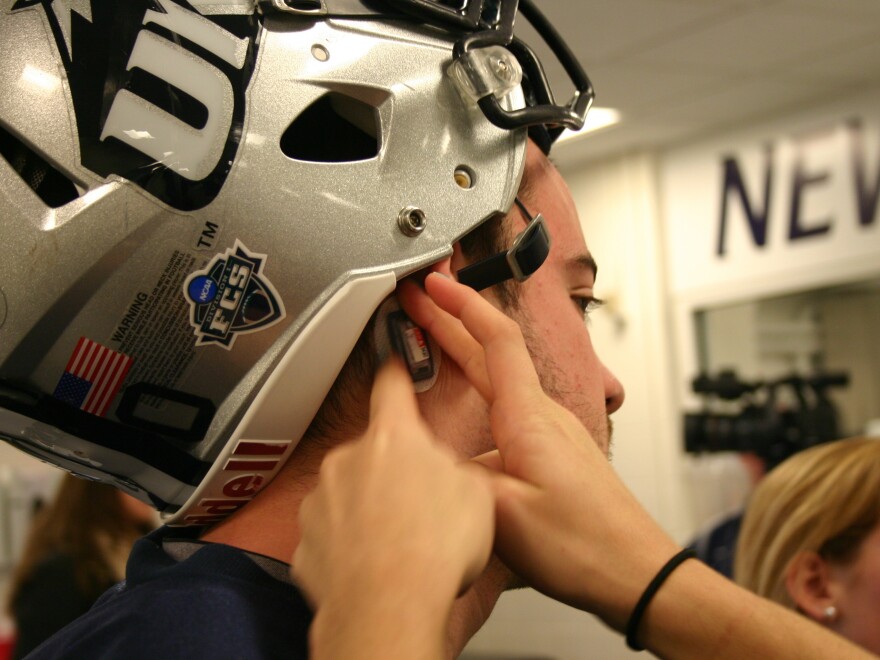 A tiny sensor is placed behind the ear of a University of New Hampshire football player. These sensors track the force and frequency of hits to the head during play.