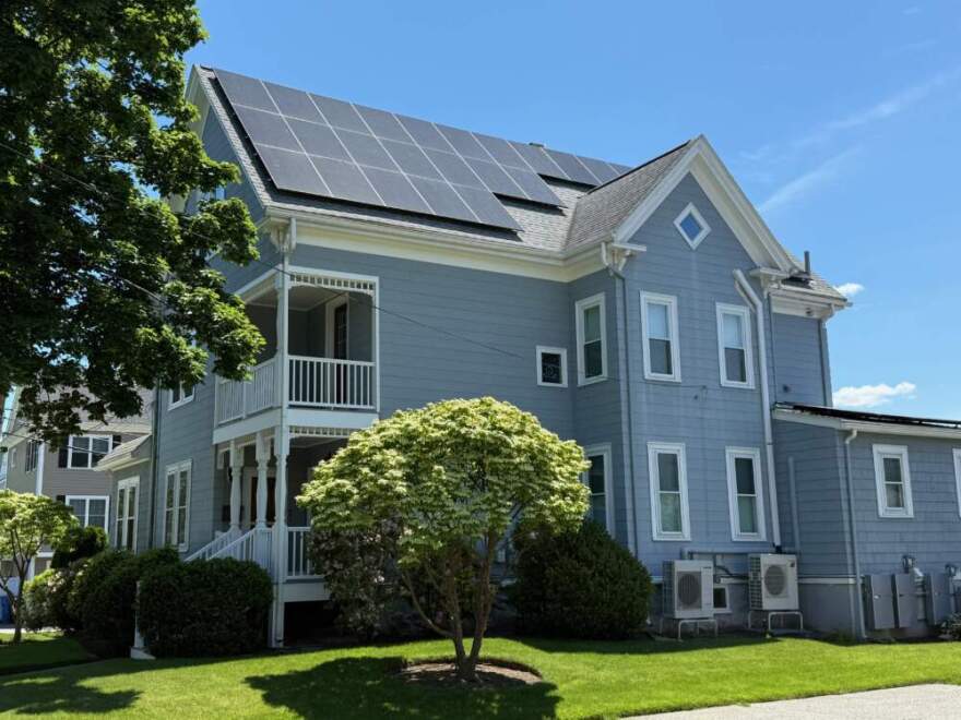 Solar panels are visible on a large blue house with white trim, surrounded by a well-tended green lawn.
