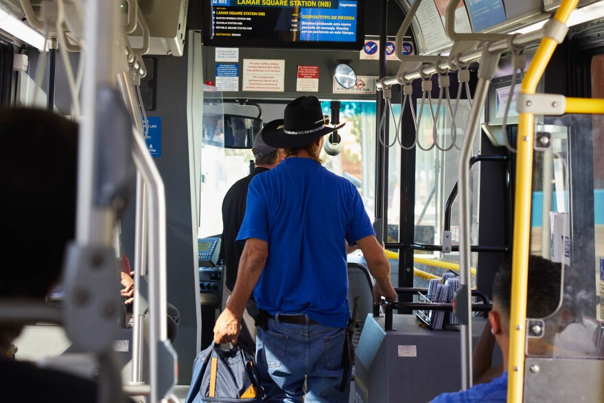 Passengers walk off of a CapMetro bus in Austin, TX on July 8th, 2022. A man in a cowboy hat and blue polo shirt is carrying a backpack as he disembarks. The view is from inside the bus looking forward, so we don't see any faces.