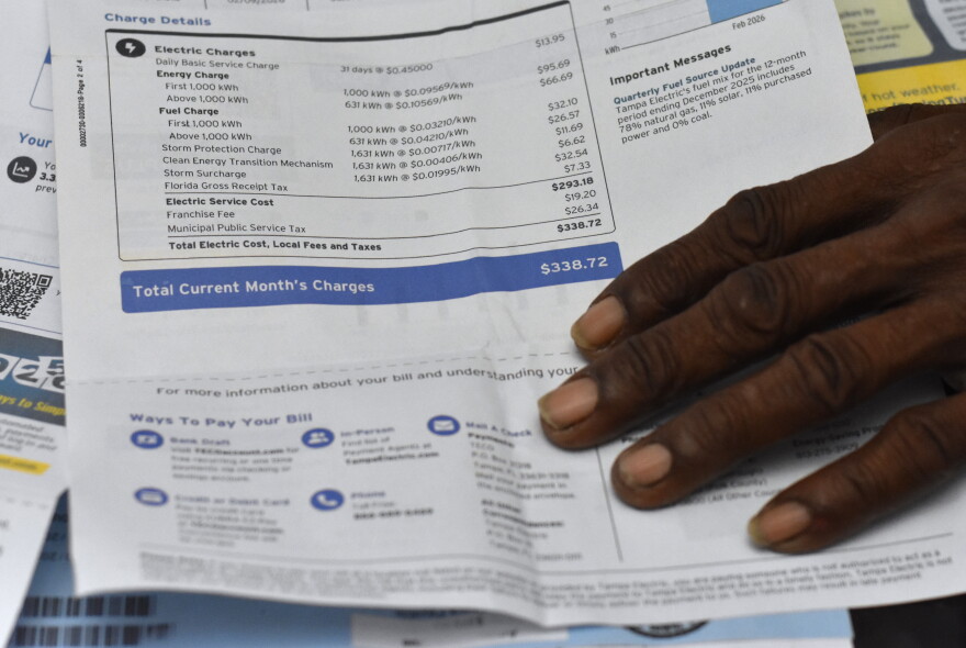An up-close photo of a Tampa Electric Power bill shows charges totaling $338 with a man’s hand resting on the bottom of the page.