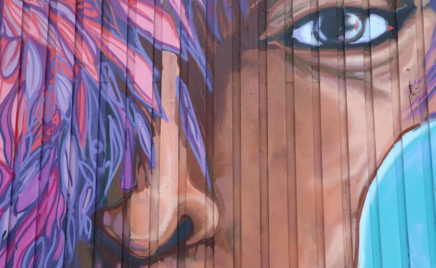 Using spray paint and brush strokes, Isaiah Williams uses a lot of bold colors and depicts several human faces.