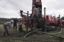 Multiple people stand around a large machine in a rural area.