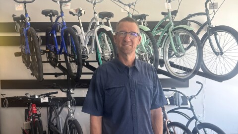 A man in a short-sleeved, blue button-down shirt stands in front of a two-tiered bicycle display.