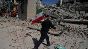 A man carries an Iranian flag to place on the rubble of a police facility struck during the U.S.–Israeli military campaign in Tehran, Iran, Wednesday, March 4, 2026. (AP Photo/Vahid Salemi)
