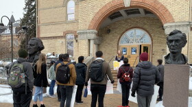 A small group of students standing outside Old Main building at USU holding signs, with one person on the steps talking to the group.